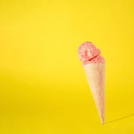 Cone with melting pink scoop of ice cream on yellow background