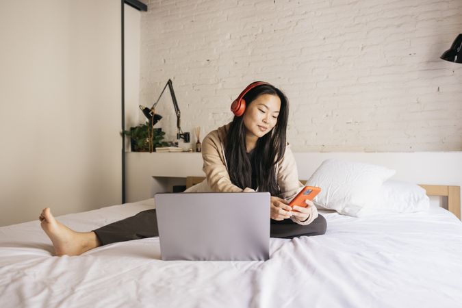 Young female using laptop and phone on bed