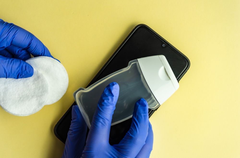 Top view of yellow table with hands wearing protective blue gloves with soap, phone and cotton