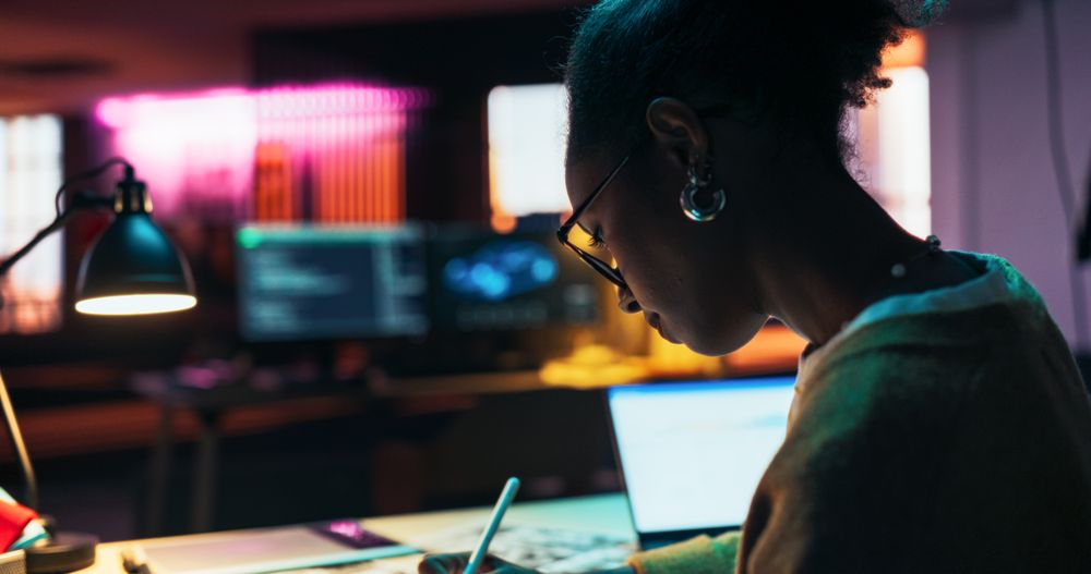 Motivated Black Female Using Laptop and Tablet Computer in Creative Agency in the Evening.