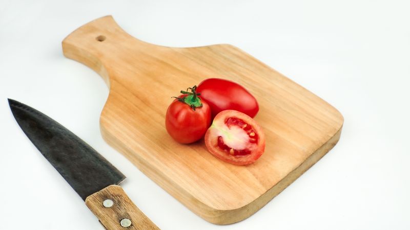 Pile of tomatoes on a wooden board some sliced with a knife