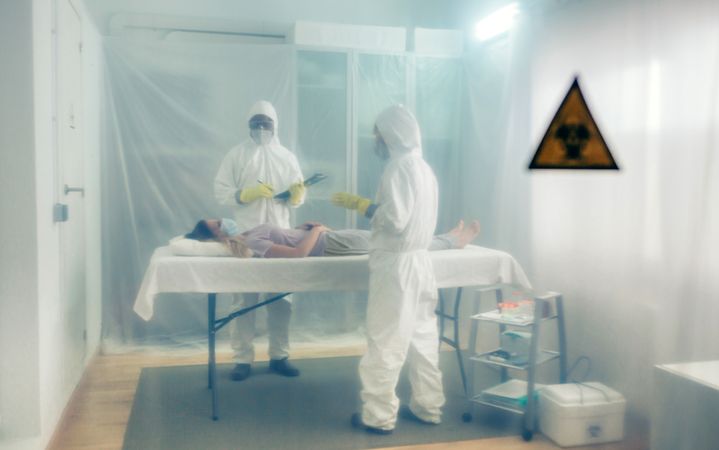 Doctors in bacteriological protection doing medical check to patient lying on a gurney