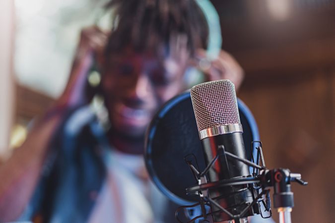 Condenser microphone with antipop filter in front of the blurred face of an Black man singing