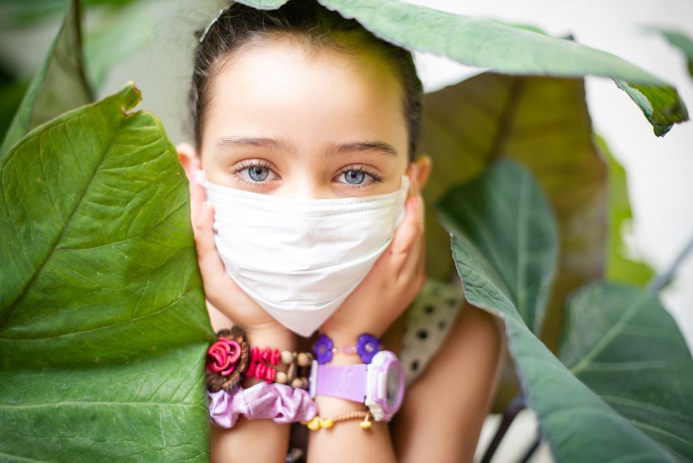 Portrait of a girl in with a face mask  surrounded by green leaves