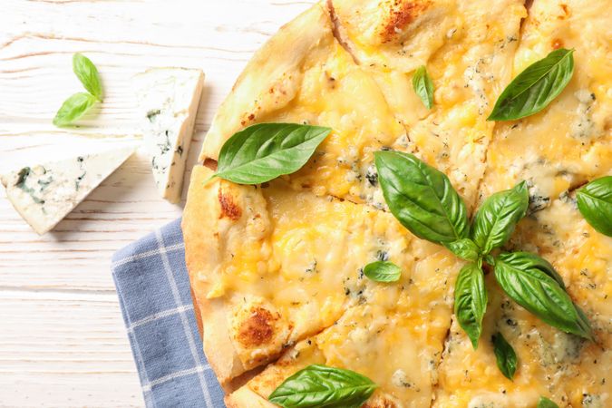 Cheese pieces and pizza with basil on neutral background, close up