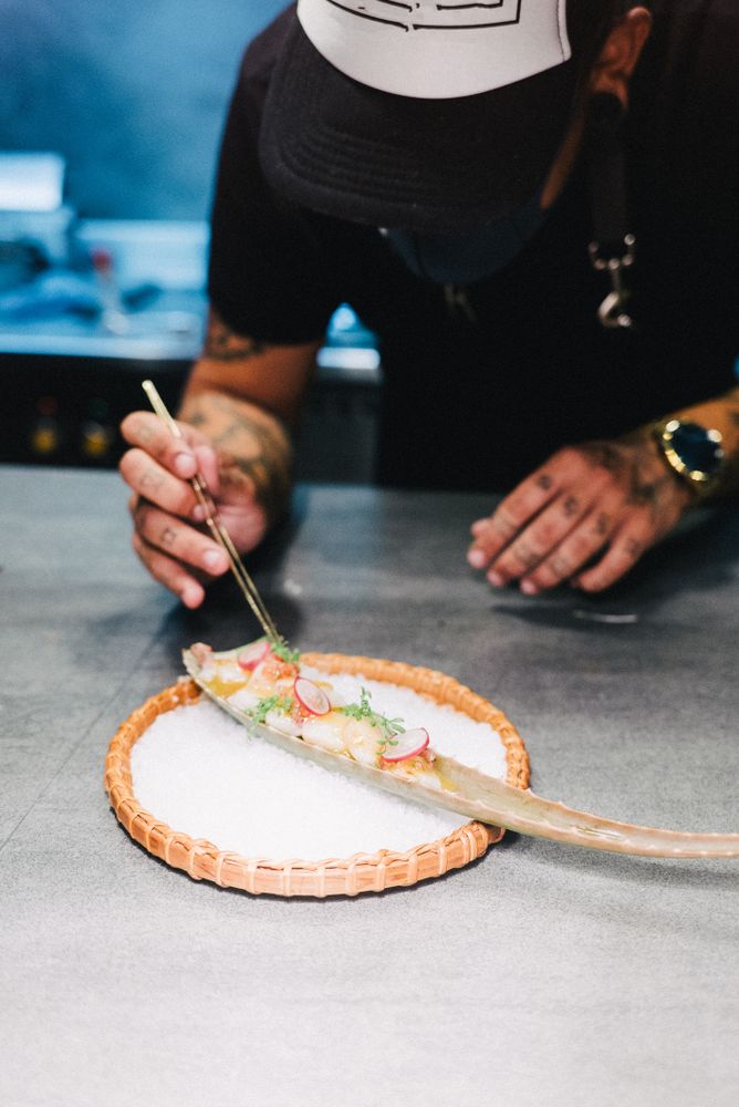 Tattooed chef putting herbs on seafood dish