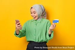 Happy Muslim woman in headscarf and green blouse receiving good news on her smart phone 4dwOl5