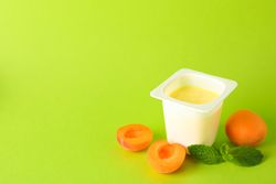 Plastic cup with yogurt and fruits on color background, space for text