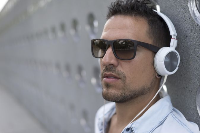 Man leaning back on wall while listening to something on headphones