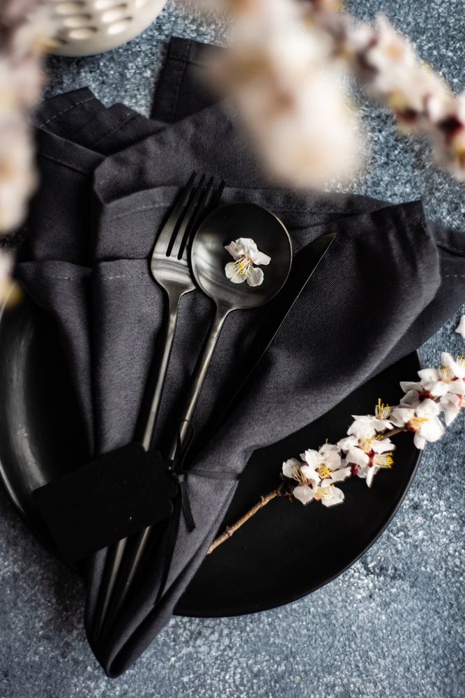 Spring floral concept with top view of apricot blossom branch on dark plate & cutlery