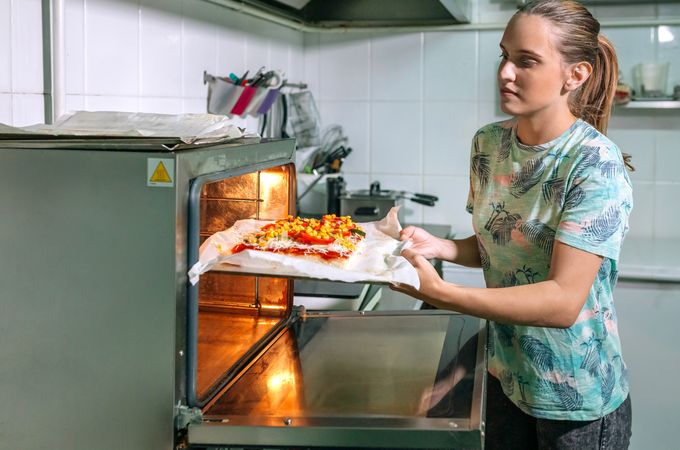 Professional cook putting pizza into oven in restaurant kitchen