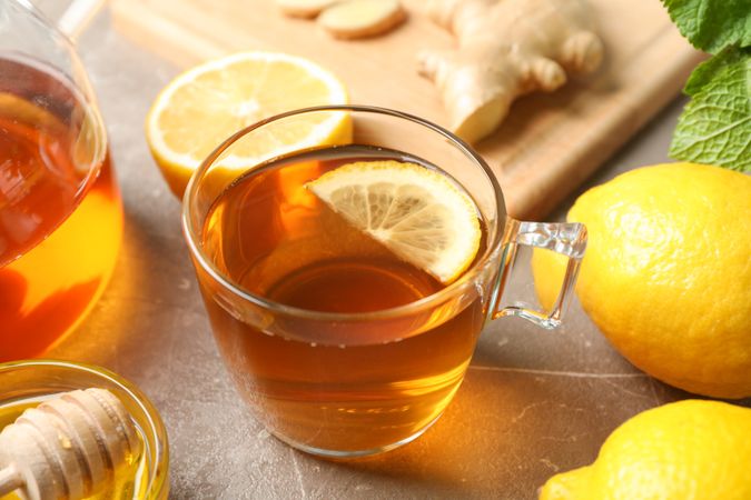 Cup of tea, mint, honey, ginger and teapot on grey background, close up