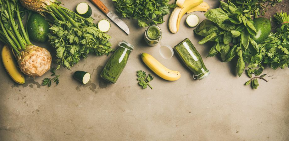 Green smoothie ingredients laying on grey background, wide composition with copy space