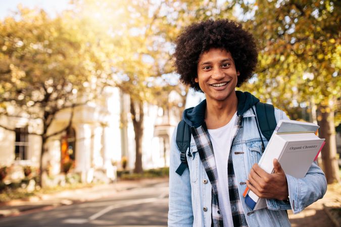Young male university student holding book on college campus