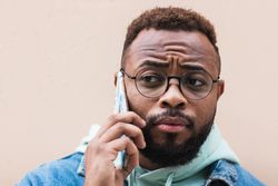 Black man talking on phone near wall