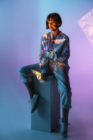 Trendy female sitting on cuboid