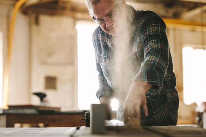 Older man cutting wood on table saw machine