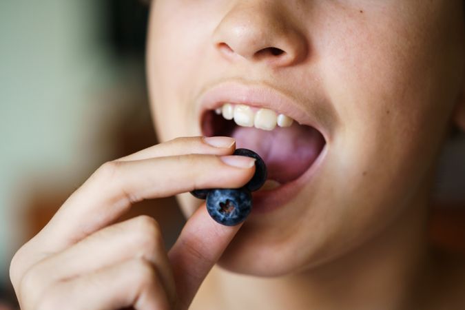 Crop of girl with mouth open eating fresh blueberries