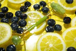 Top view of blueberries and lemons soaking in water with green jade roller