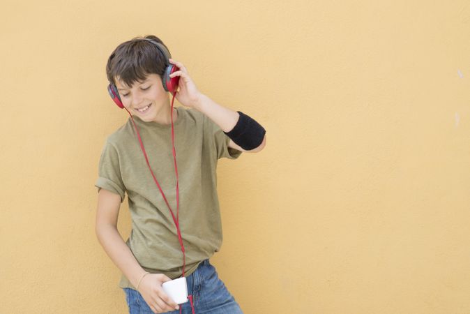 Happy teen wearing a green T-shirt listening to music on red headphones