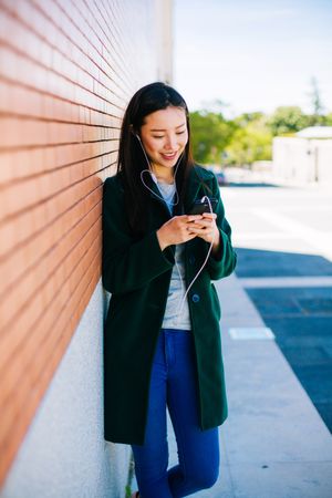 Asian female listening to music near brick wall