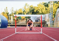 An athletic woman jumping hurdles on an athletics track.