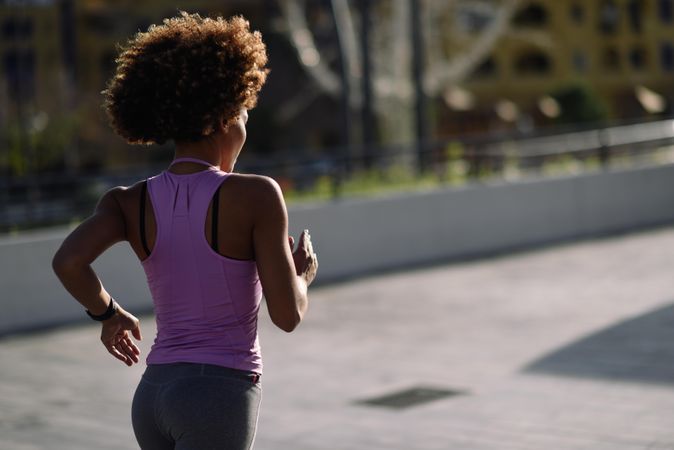Back of woman with afro hairstyle running outside on pavement in city