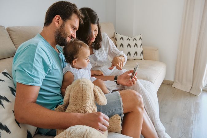 Happy parents with baby using smartphone on sofa