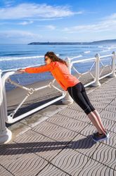 Woman stretching body on rail in front of ocean