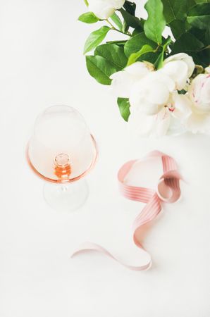 Glass of pink rose wine in the center with flowers and ribbon