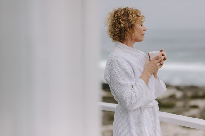 Woman enjoying coffee standing in the balcony of a beach house