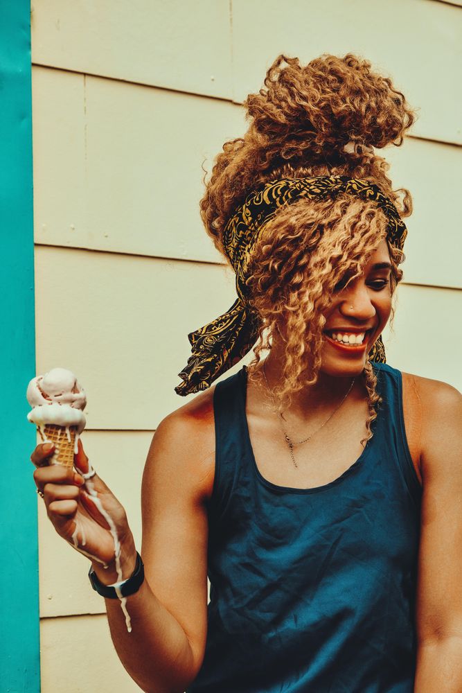 Happy Black female enjoying an ice cream cone in the sun, vertical
