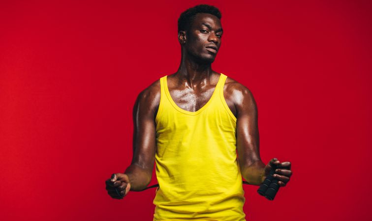 Fit young man with jumping rope on red background
