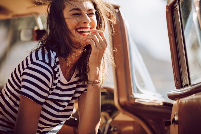 Woman in striped shirt laughing and sitting in vintage car