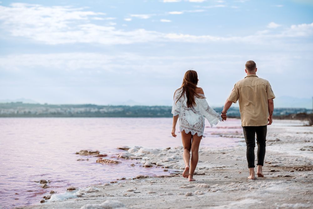 back view of adorable couple walking on an amazing beach with pink water
