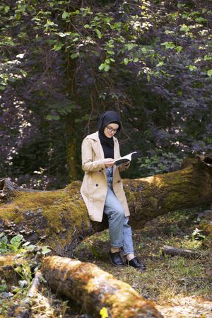 Middle Eastern woman leaning on fallen tree with book