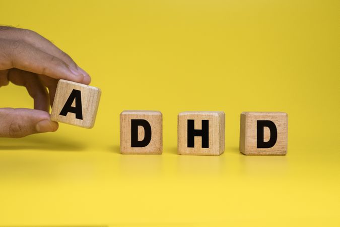 male hand put wooden blocks with ADHD or attention deficit hyperactivity disorder symbol isolated on yellow background