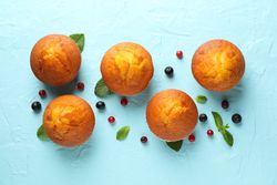 Composition with muffins and berries on blue background, top view