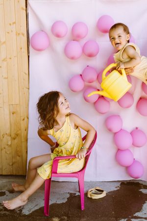 Kids having fun with watering can against wall with balloons