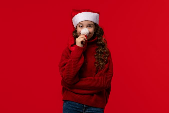 Playful girl in Santa hat holds pom-pom to nose