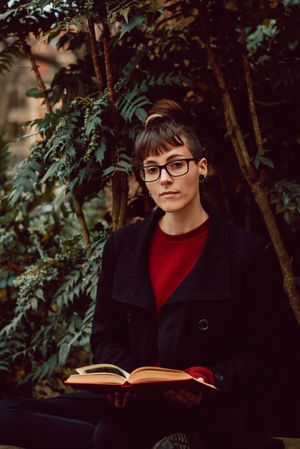 Young woman reading book on bench in park