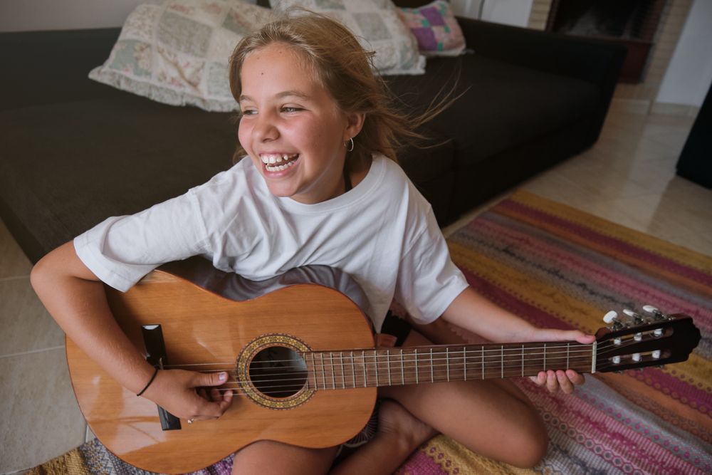 Girl sitting on the floor of a house playing a guitar and singing with happy expression