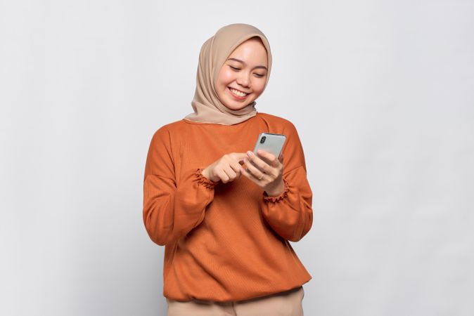 Smiling Muslim woman smiling while typing on her smartphone