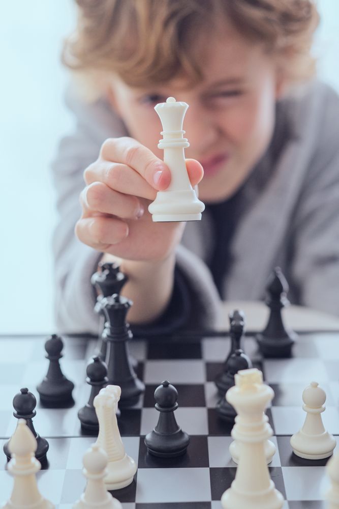 Preteen boy squinting and showing chess of piece queen