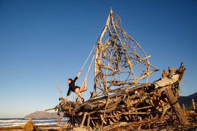 Young woman with upped leg on decorative wooden ship near water on shore