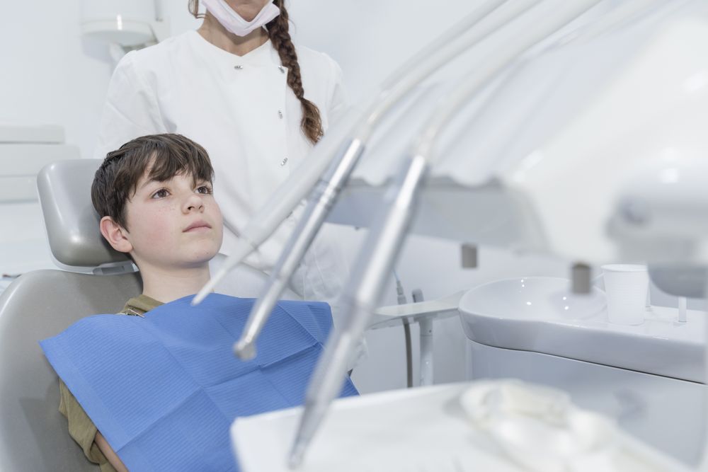 A portrait of a male teenage dental patient with female dentist standing behind chair