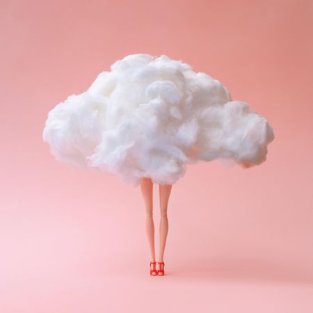 Doll with head in the clouds against pastel coral color background