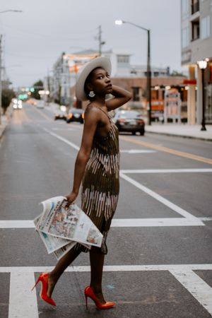 Woman in red heels holding a newspaper walking across the crosswalk in the city