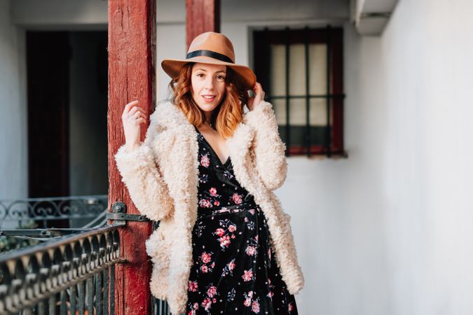 Smiling woman in warm wear standing near building and fence