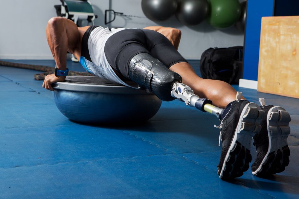 Man with prosthetic leg  exercising on rubber ball